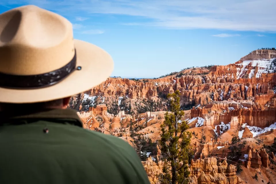 Close-up of park ranger in green jacket and khaki hat looking out at Bryce Canyon National Park red rock formations.
